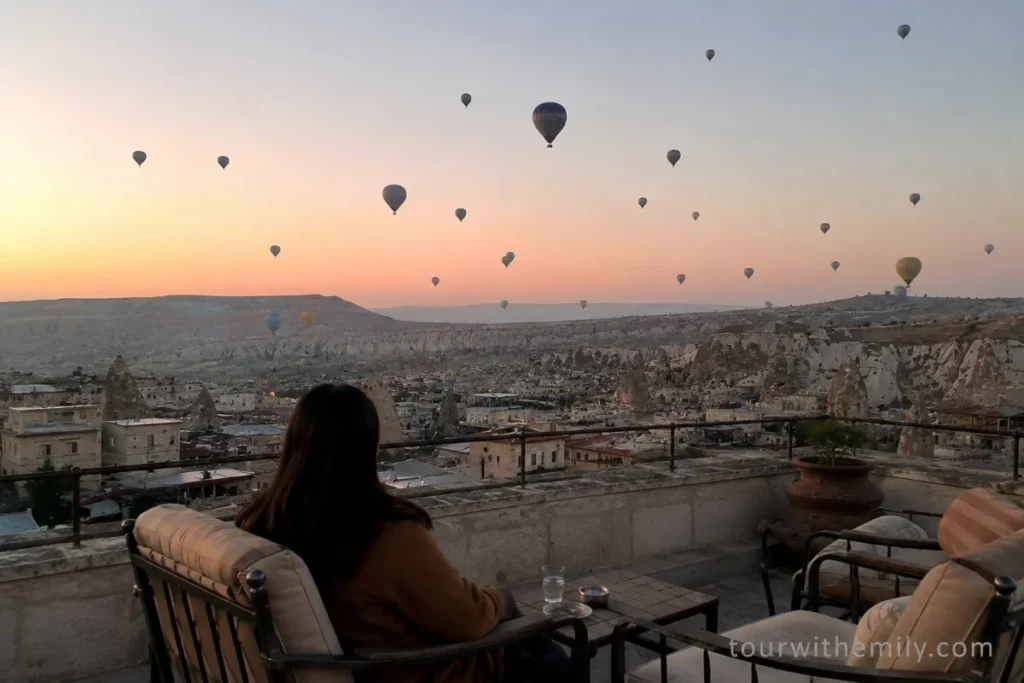 Hotel rooftop terrace in Cappadocia at dawn with hot air balloons rising over the valley and fairy chimneys in the background