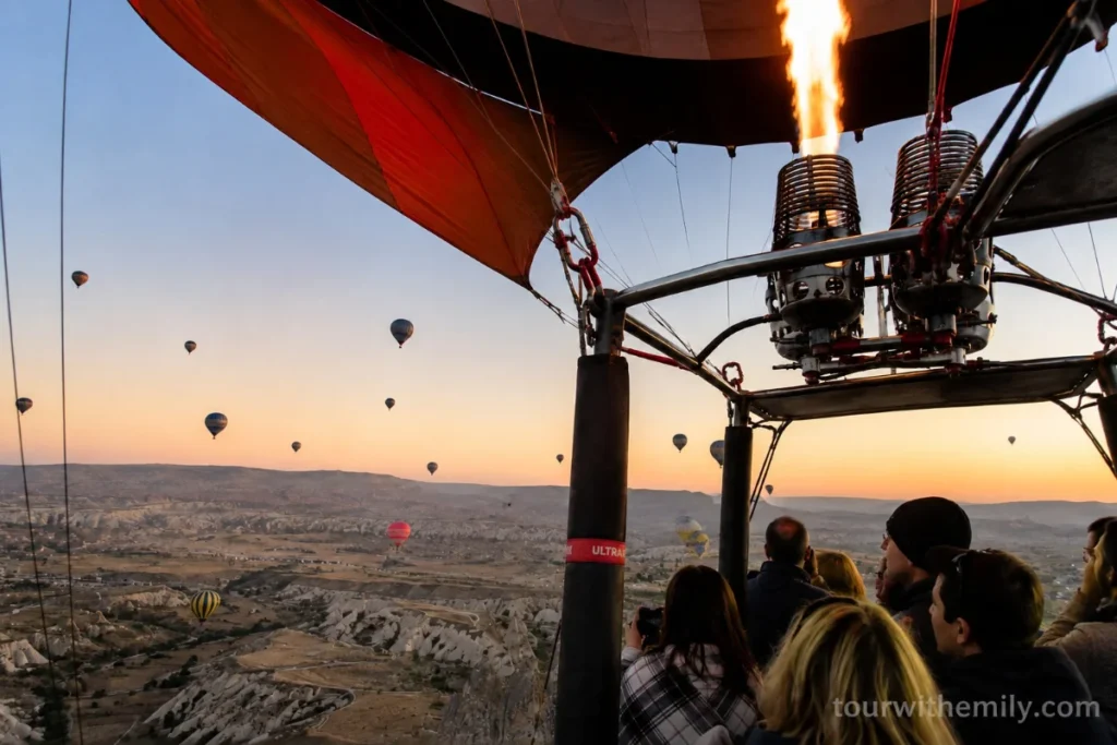 Hot air balloon over Cappadocia at sunrise with fairy chimneys and valleys below