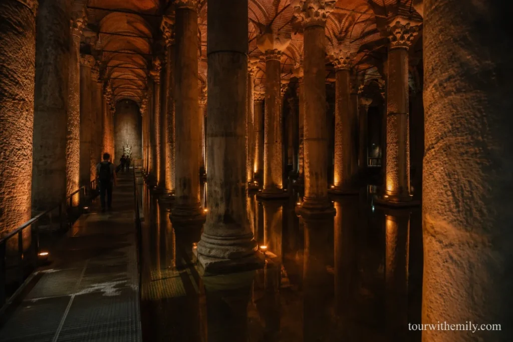 Ancient marble columns rising from shallow water inside the dimly lit Basilica Cistern in Istanbul with amber lighting reflecting on the water