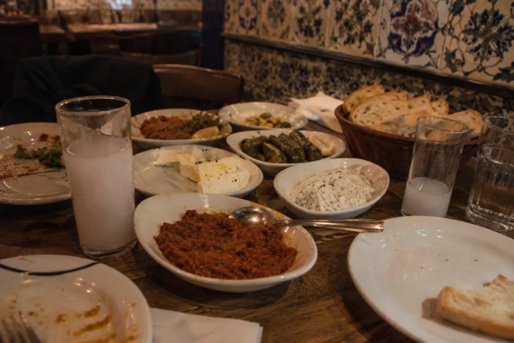 Traditional Istanbul meyhane table with raki glasses, cold meze dishes, and warm ambient lighting in a tiled interior restaurant