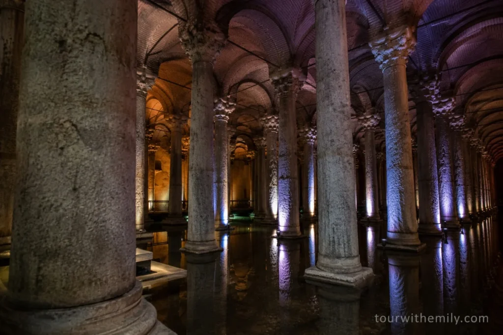 Tall columns with Corinthian capitals inside the Theodosius Cistern in Istanbul with moody lighting and brick vaulted ceiling