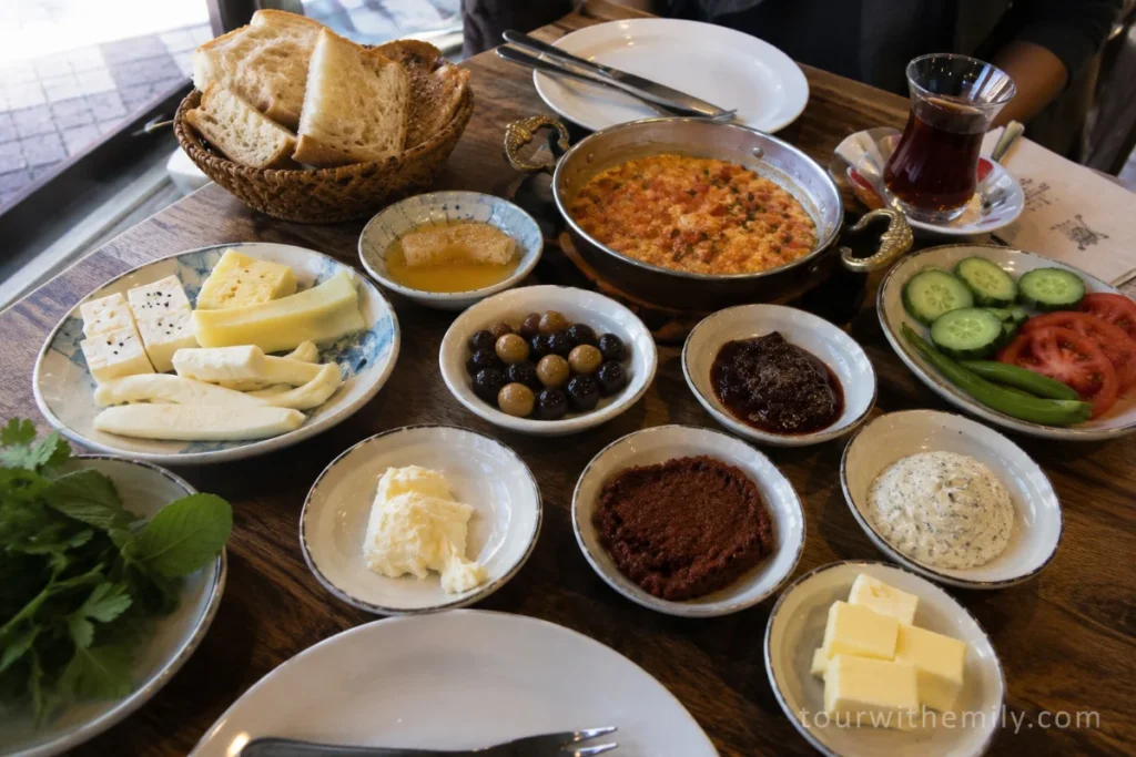 Traditional Turkish breakfast spread with multiple small dishes including cheese, olives, tomatoes, eggs, honey and kaymak on a wooden table in Istanbul