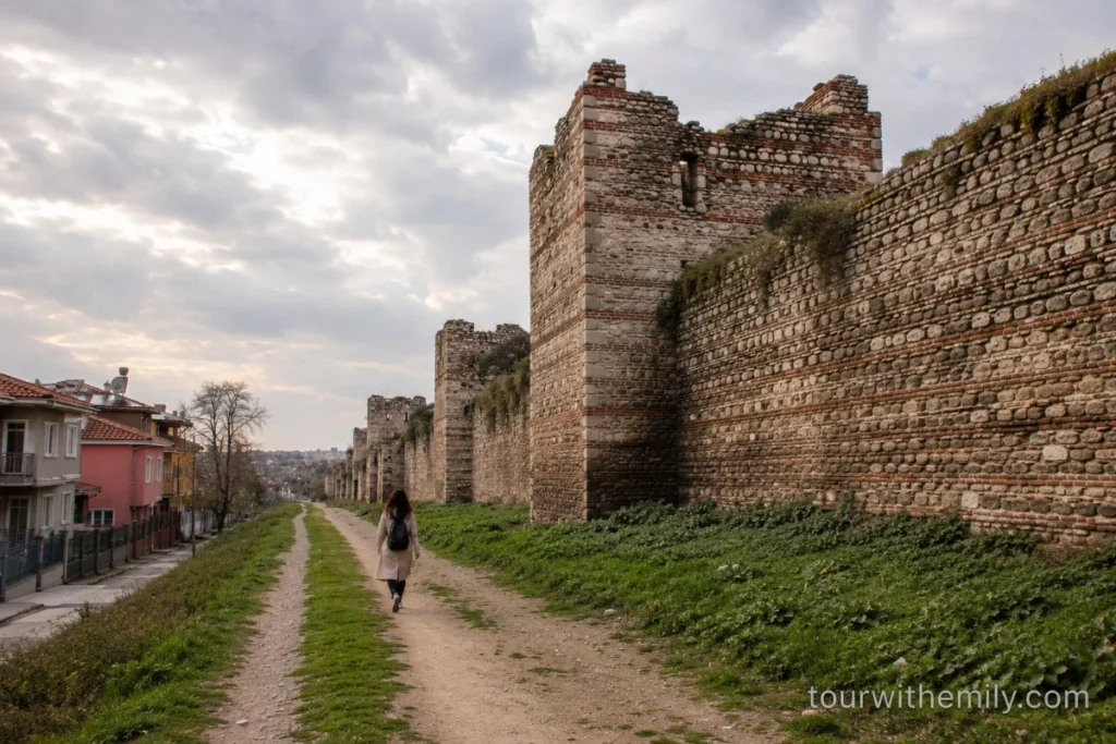 A section of the ancient Theodosian Walls in Istanbul with weathered stone towers and a walking path alongside residential buildings